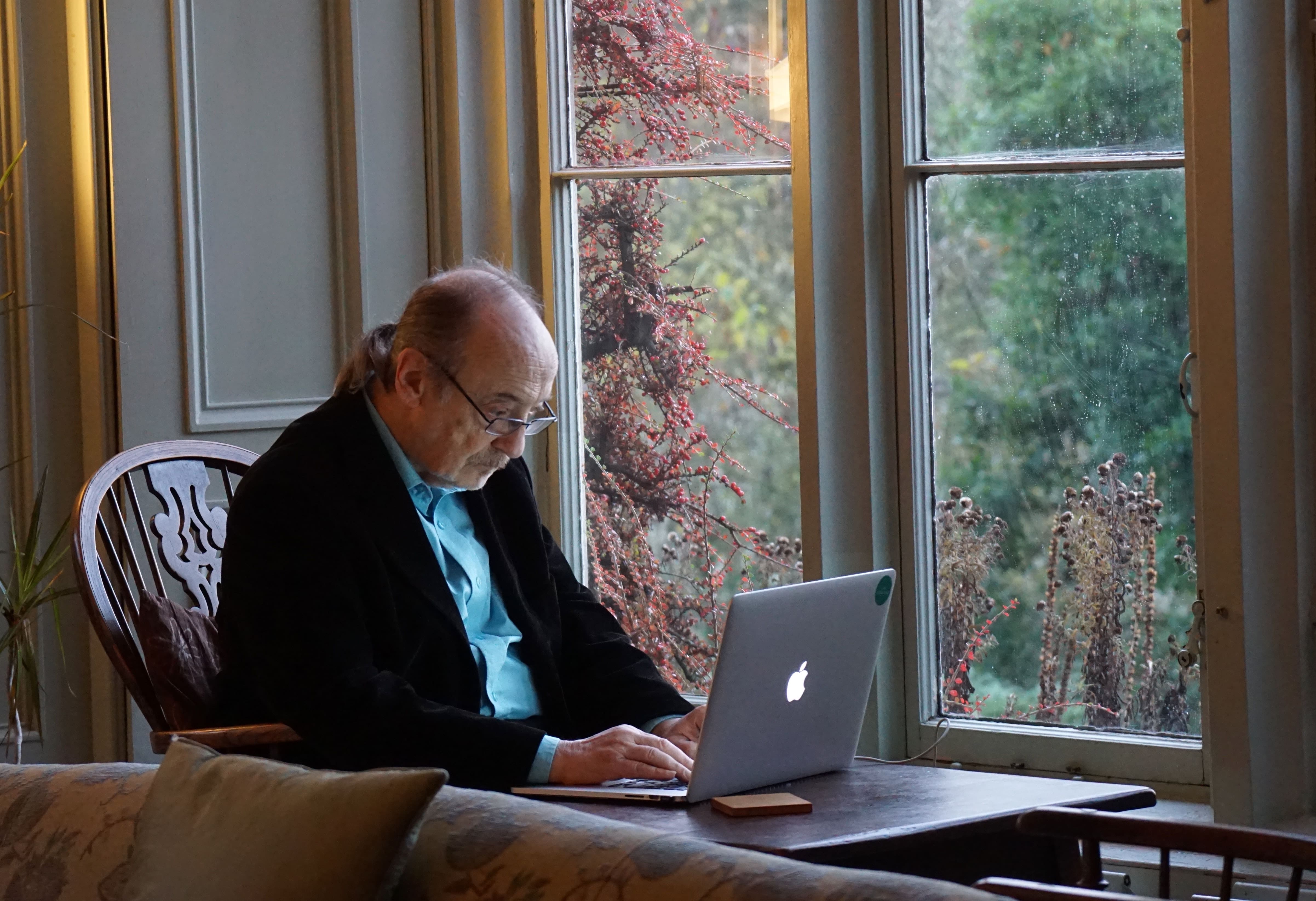 Representative image of an elderly man sitting by a window and looking at a laptop